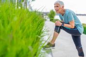 Ältere Joggerin mit kurzen grauen Haaren ist am Weg stehen geblieben und hält sich ihr linkes Bein auf einer Balustrade Ältere Joggerin mit kurzen grauen Haaren ist am Weg stehen geblieben und hält sich ihr linkes Bein auf einer Balustrade